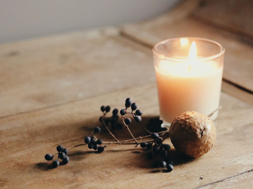 Candle in a jar with berries on a wooden board.
