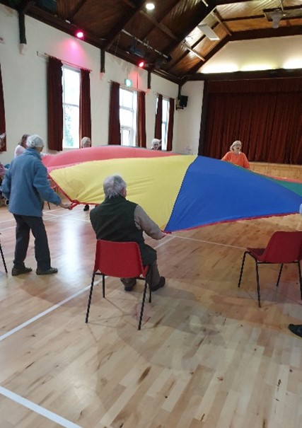 People in a community hall with a coloured parachute